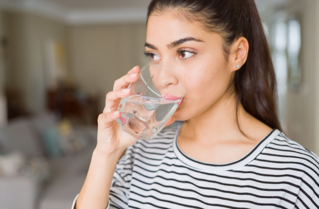 A woman in a striped shirt drinking a glass of water.