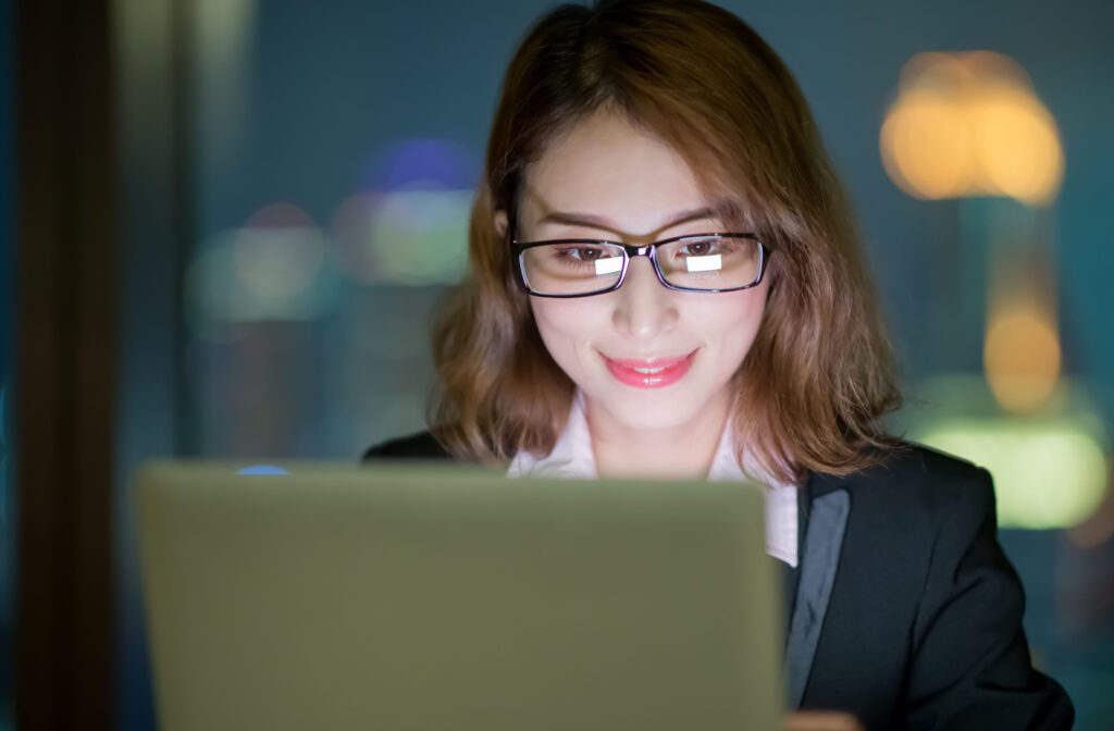 Woman wearing blue light glasses as she works in front of her computer at night.