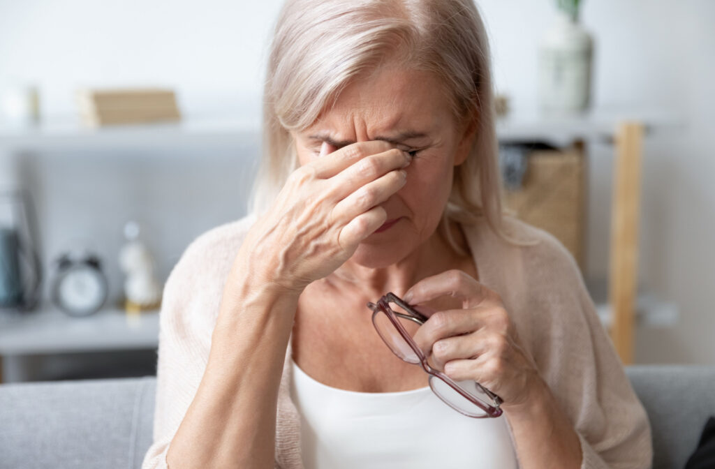 An older woman holding her glasses and rubbing her eyes in discomfort.