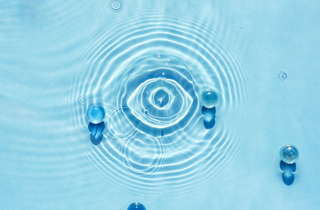 Abstract image, pool of water with water droplets that appear to form the shape of an eye.
