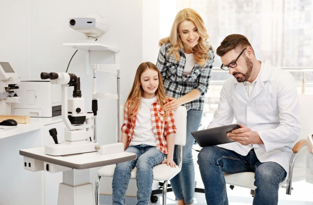 An optometrist explains the results of an eye test on dry eyes to a pre-teen and their mother in an eye exam office