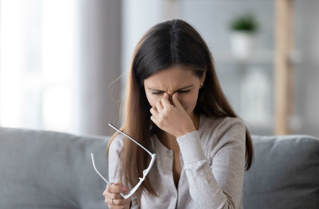 A young adult taking off their glasses and rubbing their eyes due to irritation from blocked meibomian glands.