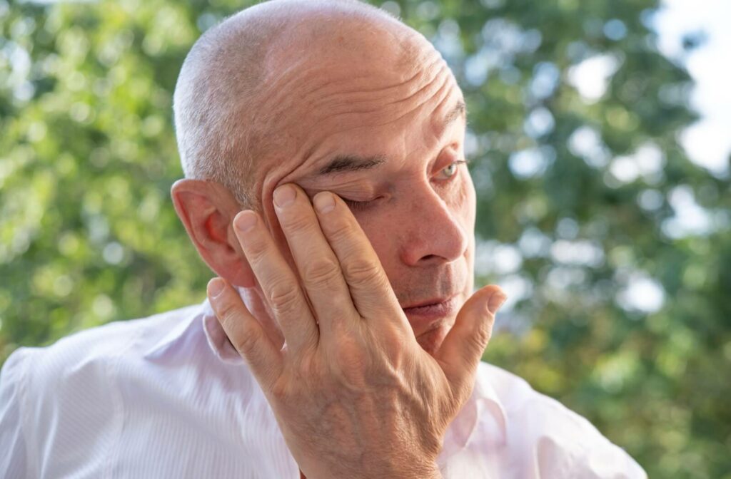 An adult outside rubbing their right eye in frustration to relieve dry eye discomfort from blocked meibomian glands.
