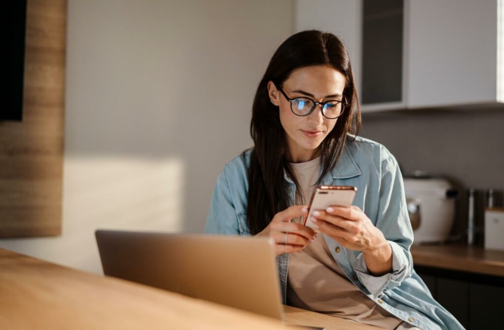 A person wearing glasses to help with their vision while looking at their phone & working at their computer