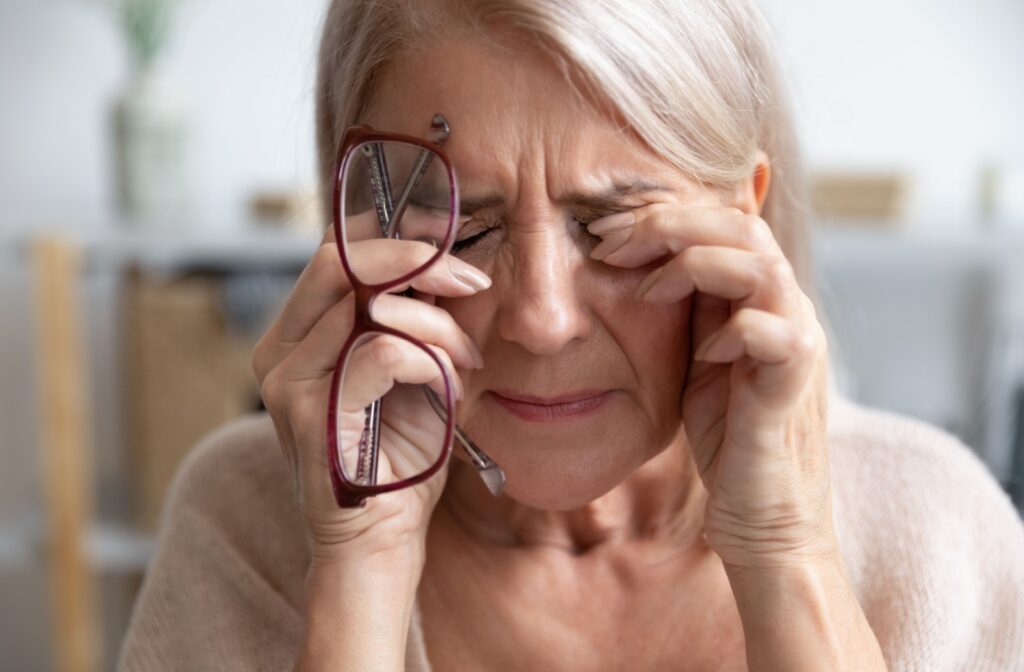 A person holding their glasses and rubbing their itchy eyes with both hands.