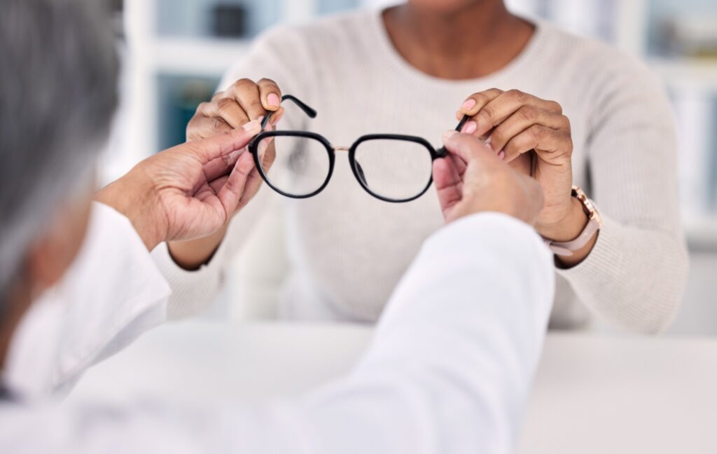 An optometrist hands their client a new pair of black glasses, perfectly fit to their client's face.