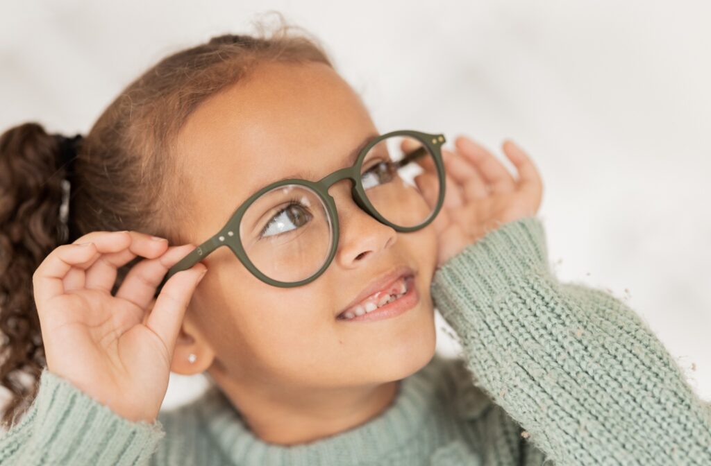 A child in a cable knit sweater wearing green glasses.