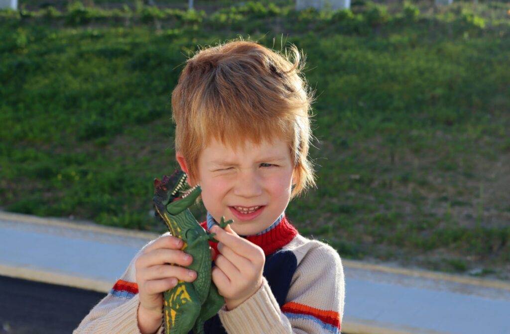A child squints while looking a dinosaur toy