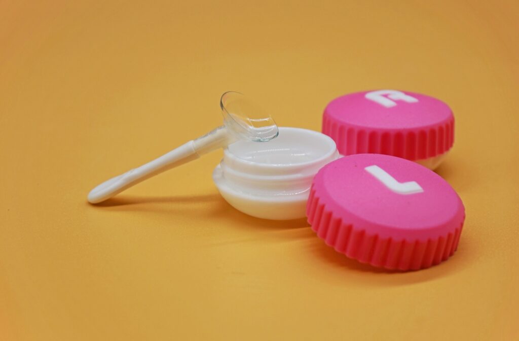 A contact lens sits on a contact lens plunger on top of a pink contact lens case
