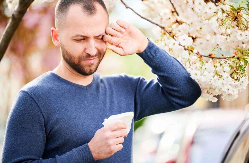 A person standing next to a blossoming tree during peak allergy season rubbing their dry eye